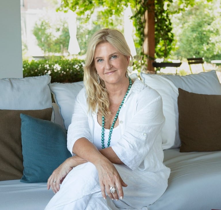Woman in white shirt sitting on cushioned sofa with blue and green pillows, smiling at camera outdoors