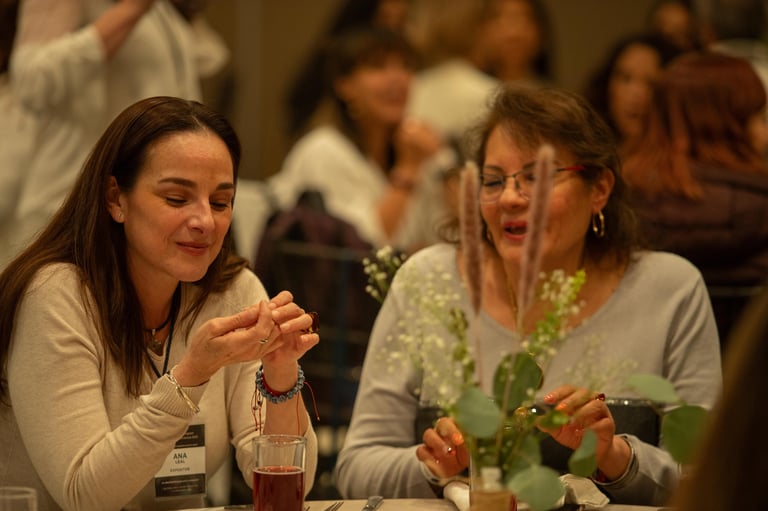 Two women smiling while having a conversation at a social gathering with other guests in the background