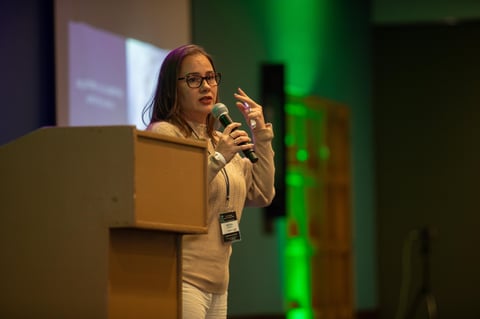 Woman with glasses speaking at podium with microphone during presentation with green stage lighting