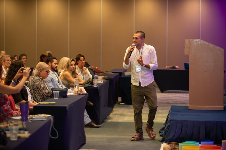 Man speaking at conference podium with audience seated at tables in hotel ballroom